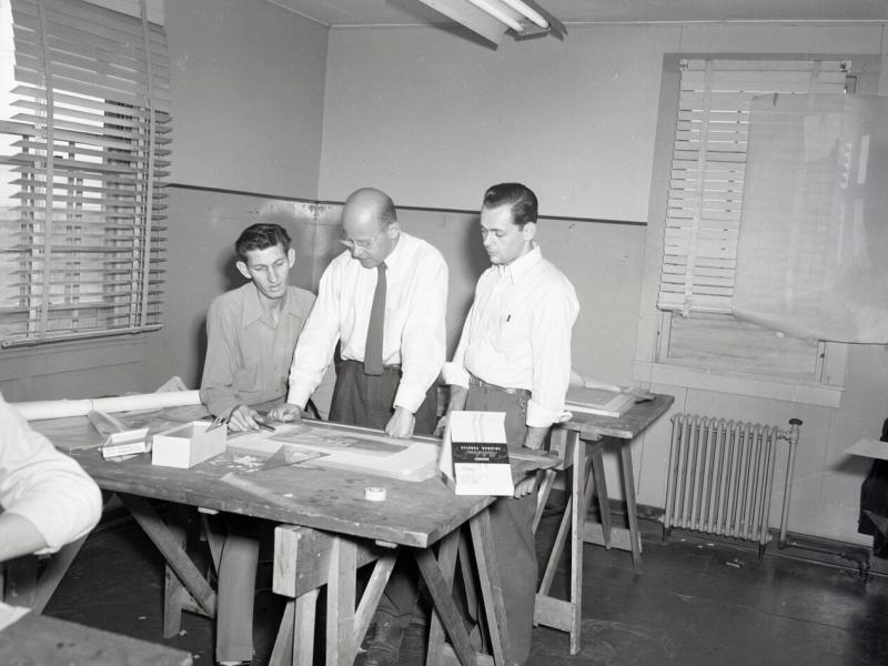 Two students discuss an architectural drawing with their professor